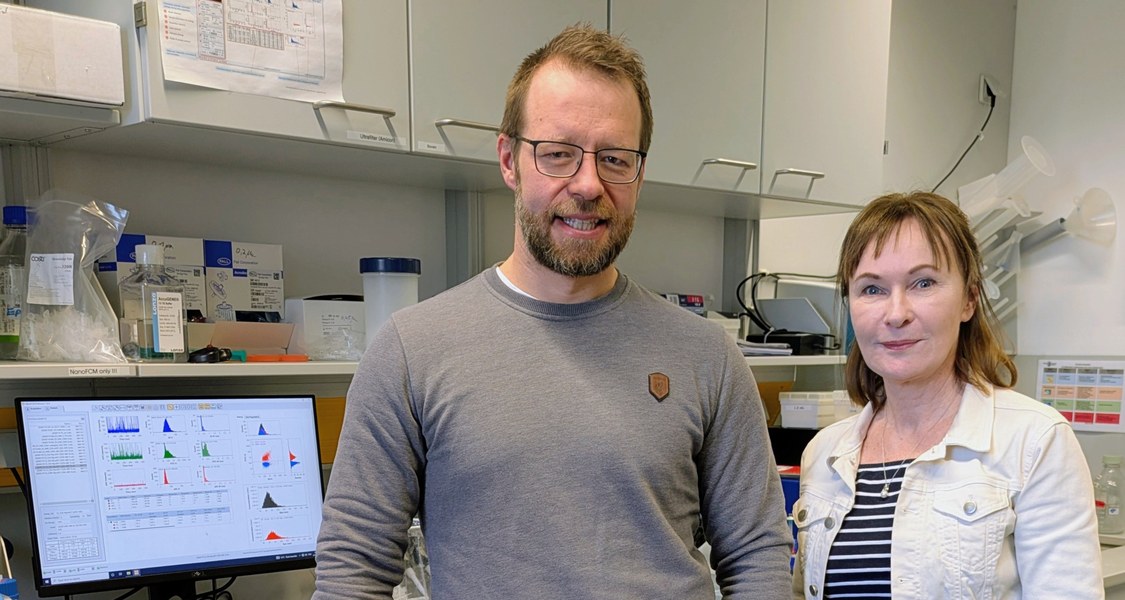 Dr. Christian Preußer (Leiter EV-iTEC Core Facility) und Prof. Elke Pogge von Strandmann (Direktorin Institut für Tumorimmunologie) stehen lächelnd nebeneinander in einem modernen Labor am Zentrum für Tumor- und Immunbiologie der Philipps-Universität Marburg. Im Hintergrund sind Labortische mit Zentrifugen, Reagenzienflaschen, Pipetten und einem Monitor mit Datenvisualisierungen zu sehen, typisch für Forschung zu extrazellulären Vesikeln und Tumorimmunologie.