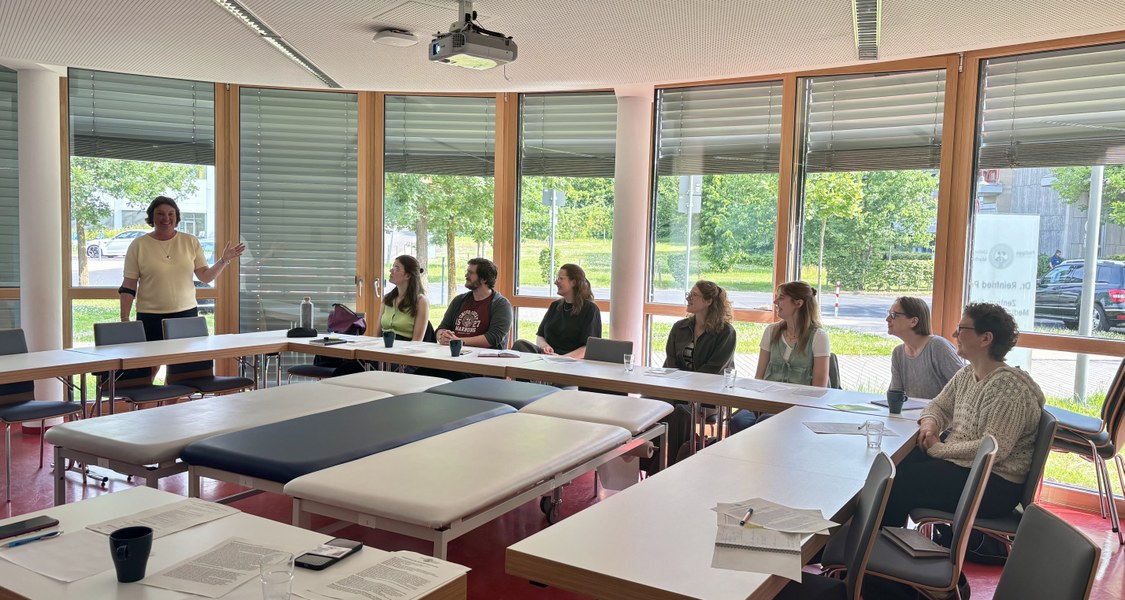 Andrea Schönbauer, stellvertretende Leiterin des MARIS, gibt den Besucher*innen Einblicke in die Ausbildungsinhalte der Schauspielpatient*innen im MARIS. Von rechts nach links zu sehen sind: Eva Maria Gauß, Prof. Dr. Kati Hannken-Illjes, Maja Ungruhe, Beata Sosnowska, Elisabeth Kleschatzky, Jonas Reiter, Elisa Zink, Andrea Schönbauer