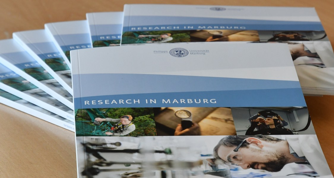Forschungsbroschüren der Philipps-Universität liegen aufgefächert auf einem Tisch