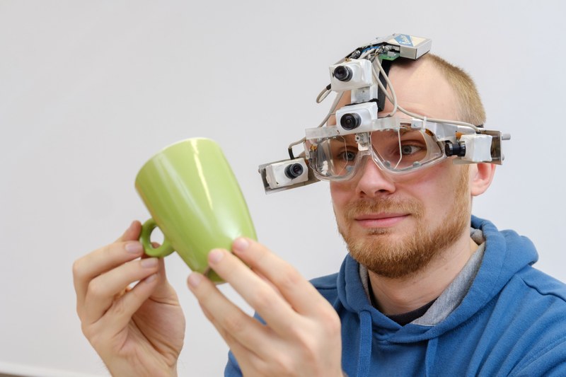 Person mit einem Eyetracker hält eine Tasse in den Händen und betrachtet diese