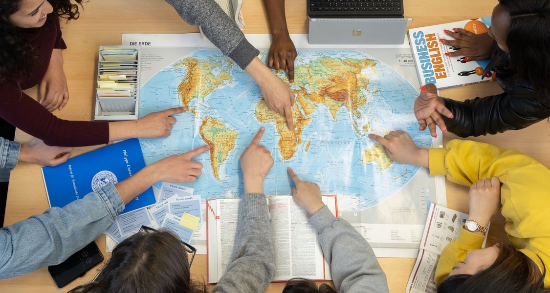 Eine Gruppe junger Menschen zeigt auf eine Weltkarte.