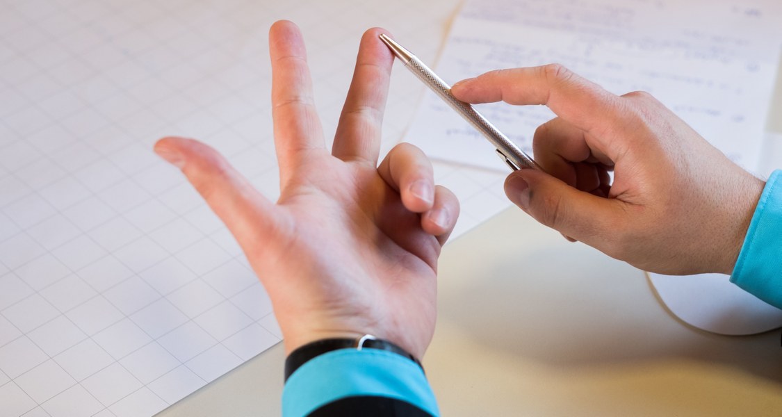 Eine Hand über einem Tisch zählt etwas an den Fingern ab