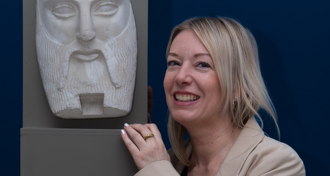 Sabine Neumann neben einer bärtigen antiken steinernen Maske.