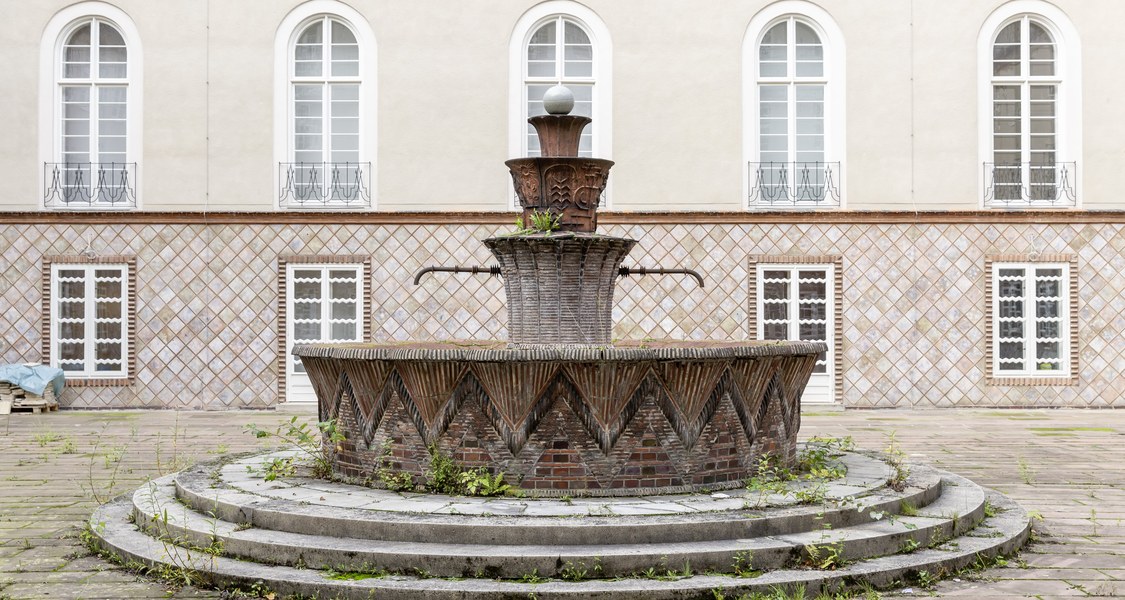 Zu sehen ist der Brunnen im Innenhof des Kunstmuseums. Einzelne Pflanzen brechen aus der Brunnenschale und sowohl Mängel als auch die einstige Schönheit wird deutlich.