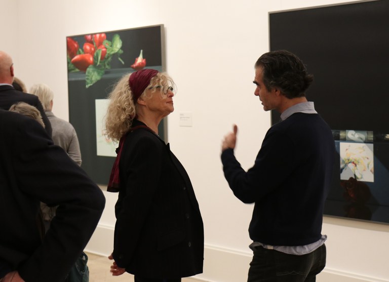 Zwei Personen unterhalten sich angeregt. Im Hintergrund sind mehrere Personen und die Kunstwerke von Rolf Gith zu sehen.