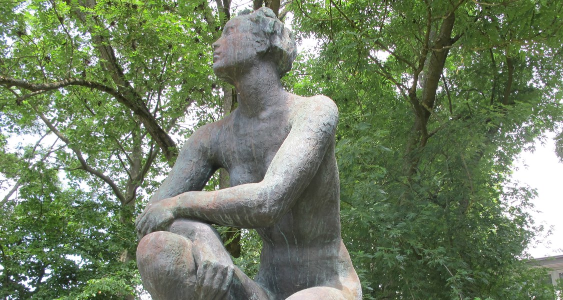 Überlebensgroße Bronzefigur im Garten des Kunstgebäudes. Zu sehen ist eine unbekleidete Frauenfigur in hockender Position.