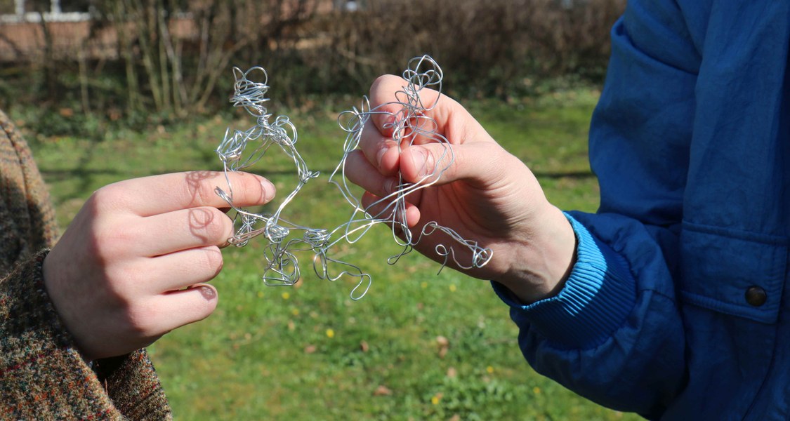 Zwei Drahtfiguren die von zwei Händen gehalten werden und sich begegnen.