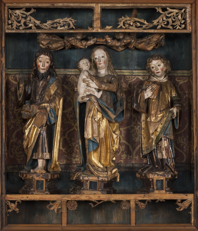 Zu sehen sind die Figuren Maria mit Kind, sowie links und rechts von ihr die eines bärtigen und eines bartlosen Heiligen. Die Figuren stehen jeweils auf einem Sockel. Oberhalb befinden sich zwei schwebende Engel.