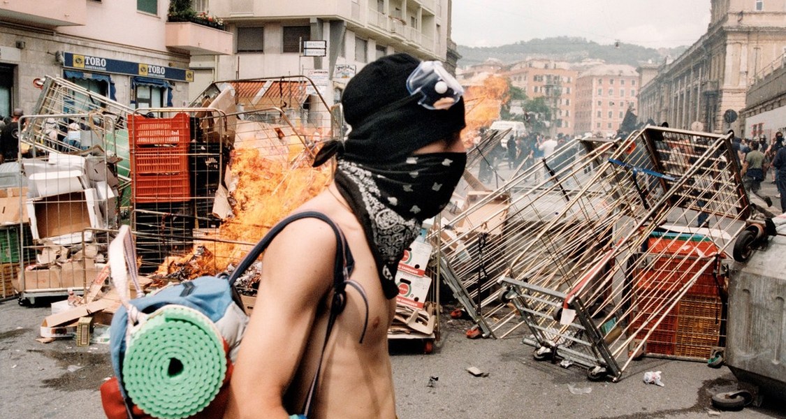 Vor einer Barrikade steht ein Protestierender mit nacktem Oberkörper und Mundschutz.