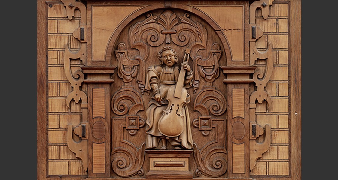 Aus Holz geschnitzte Figur, Gambe spielend, auf der Tür einer Zimmerorgel.