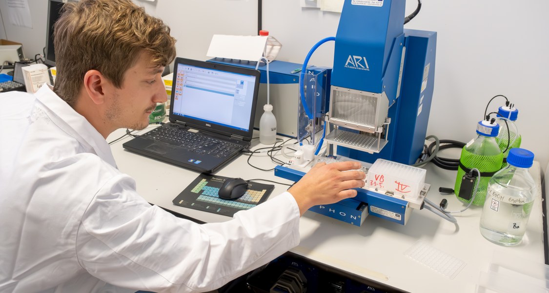 Studierender der Chemie arbeitet mit einem blauen labortechnischem Gerät, dass an einem Laptop angeschlossen ist.