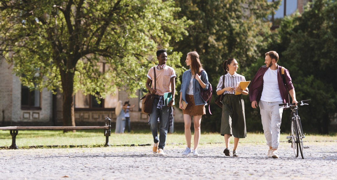 Eine Gruppe multikultureller Studierender läuft gemeinsam lachend durch einen Park.