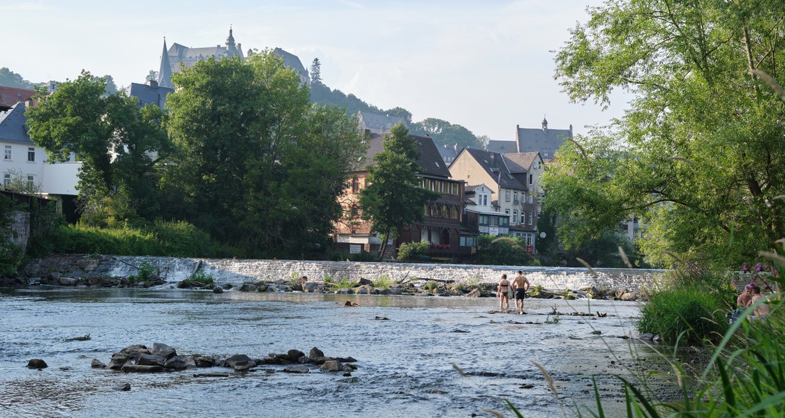 Blick auf das Marburger Wehr mit Menschen, die im Wasser waten.