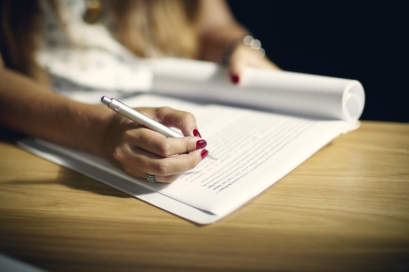 Eine weibliche Hand schreibt mit einem Kugelschreiber auf ein bedrucktes Blatt.