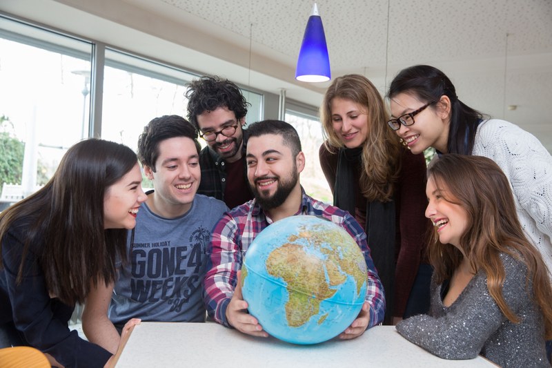 Sieben Studierende schauen lachend auf einen Globus.