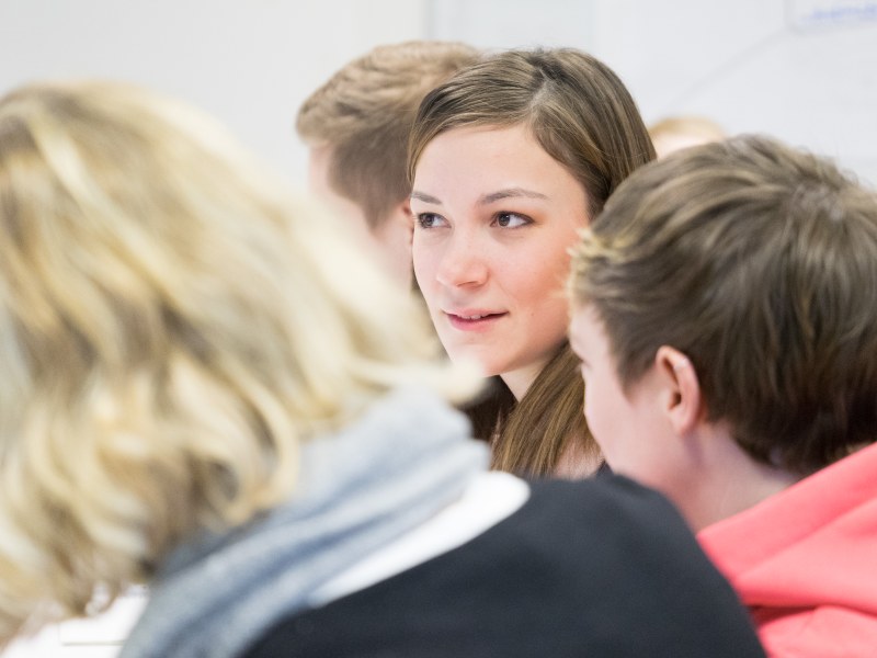 Eine Studentin sitzt in einer Gruppe von Menschen und richtet ihren Blick nach vorn.