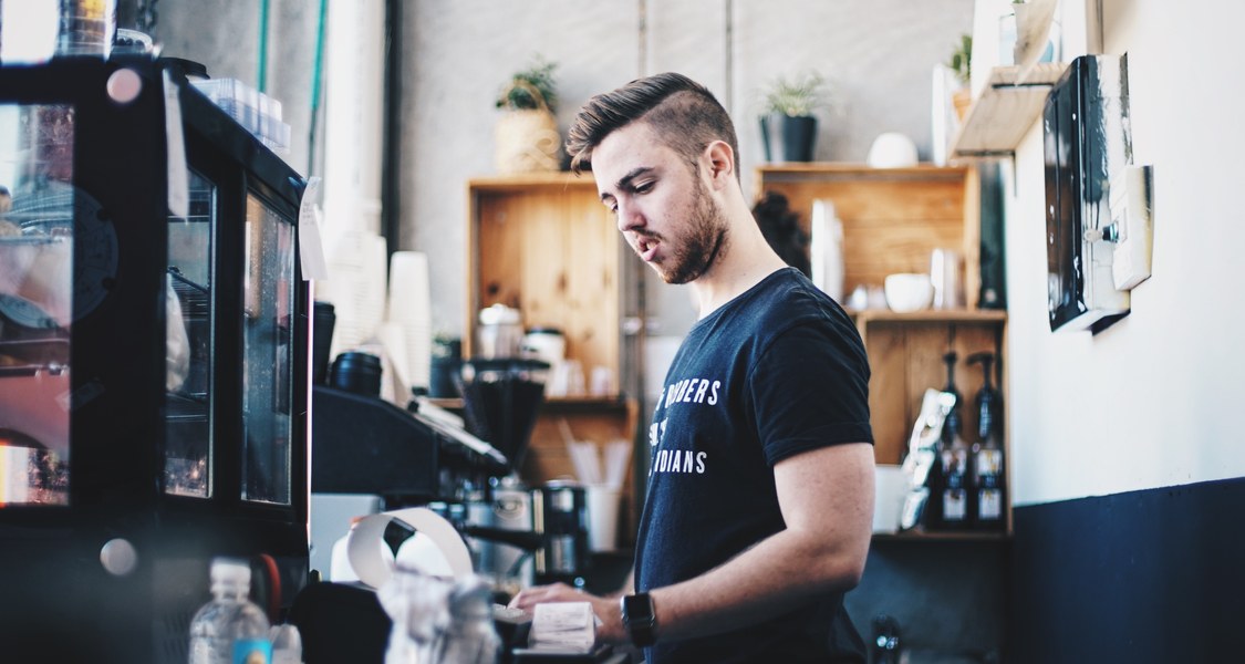 Ein junger Mann arbeitet als Barista hinter dem Tresen.