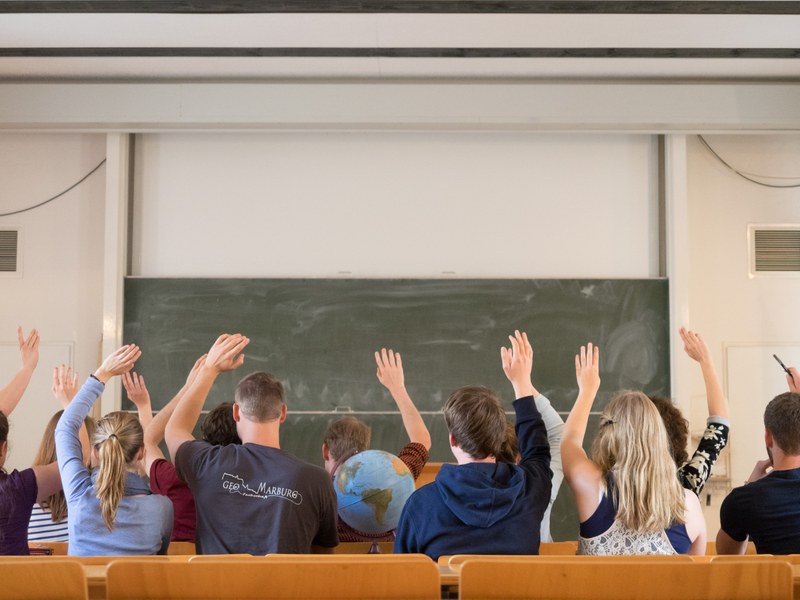 Studierende sitzen in einem Hörsaal und melden sich.