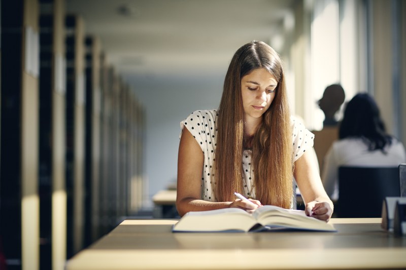 Eine Studentin sitzt konzentriert über ein Buch gebeugt in der Bibliothek des Deutschen Sprachatlas.