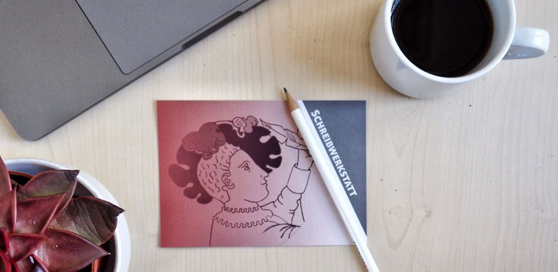 Schreibtisch mit Laptop, Kaffeetasse, Stift und Karte der Schreibwerkstatt