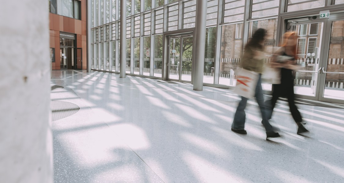 Das Foto zeigt zwei Student*innen im Foyer der Unibibliothek in einer verwischenden Fototechnik