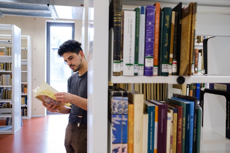 Student mit Buch zwischen Bücherregalen