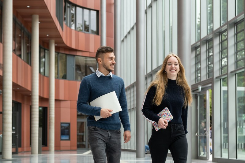 Zwei Studierende laufen im Atrium der UB auf die Kamera zu.