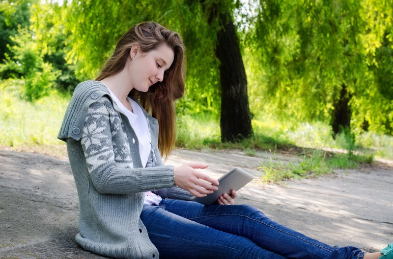 Junge Frau sitzt im Freien mit einem Touchscreen-Tablet