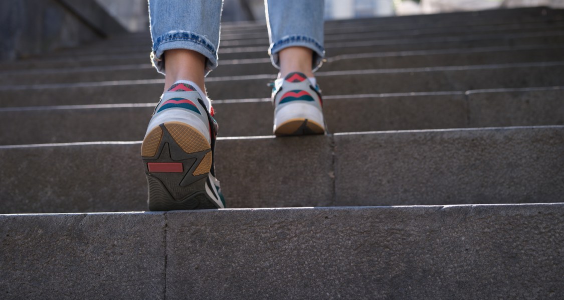 Eine Person in Jeans und Turnschuhen steigt eine Steintreppe hinauf.