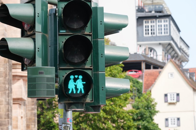 Grüne Fußgängerampel an der Alten Universität, die zwei Figuren in Kleidern zeigt, die sich an der Hand halten.