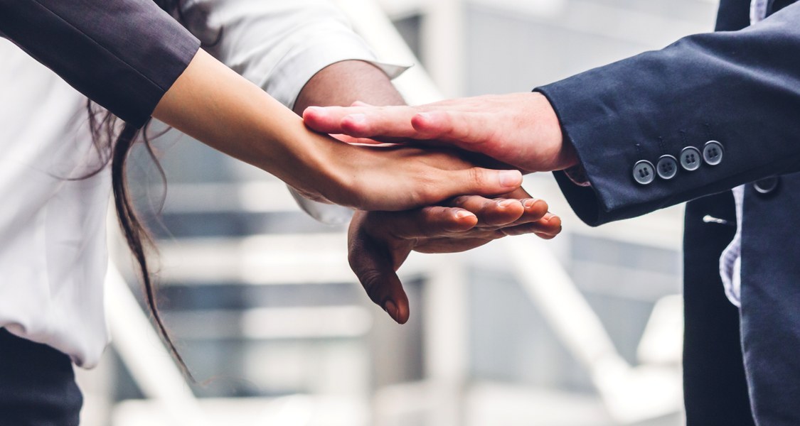 Drei Personen legen die Hände übereinander (Ausschnitt Arme)