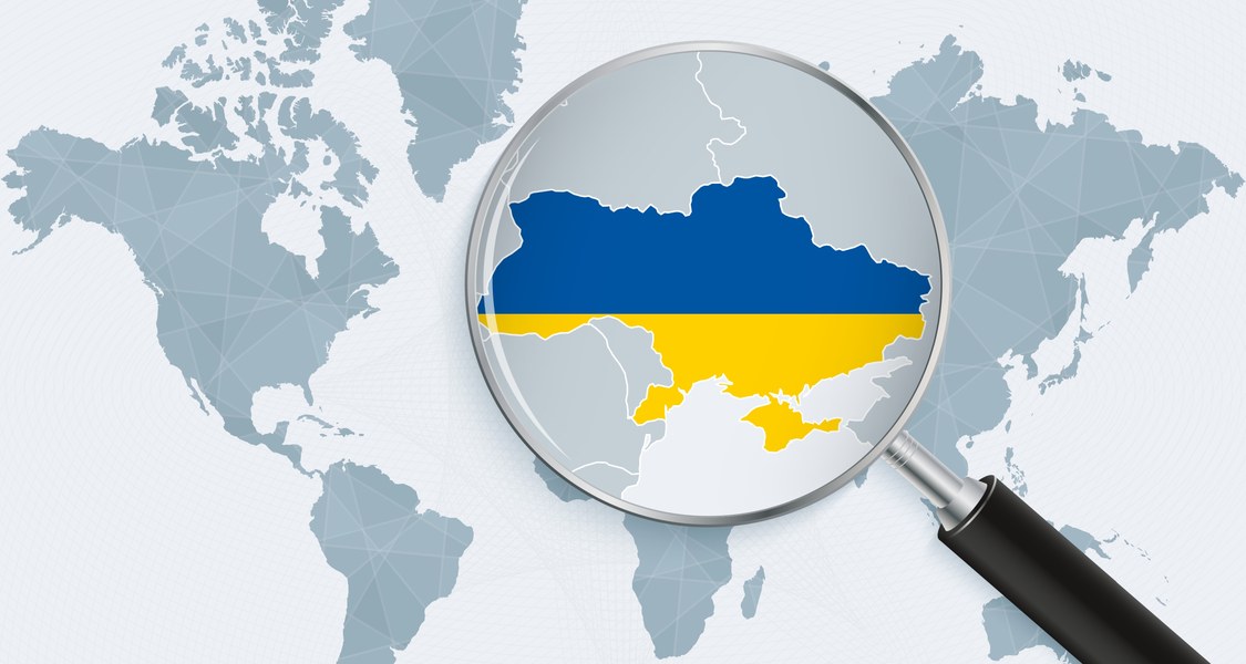 Weltkarte mit einer Lupe über der Ukraine in Landesfarben
