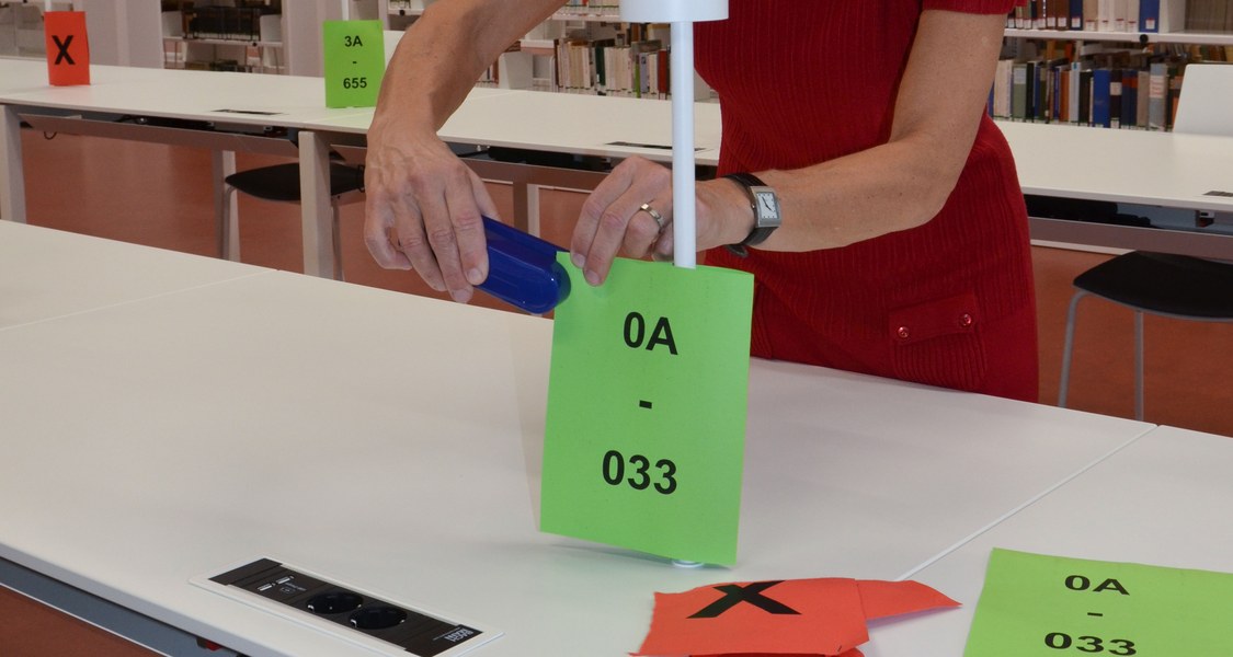 Ein Mitarbeiterin der UB befestigt grüne und rote Fahnen an den Arbeitsplätzen
