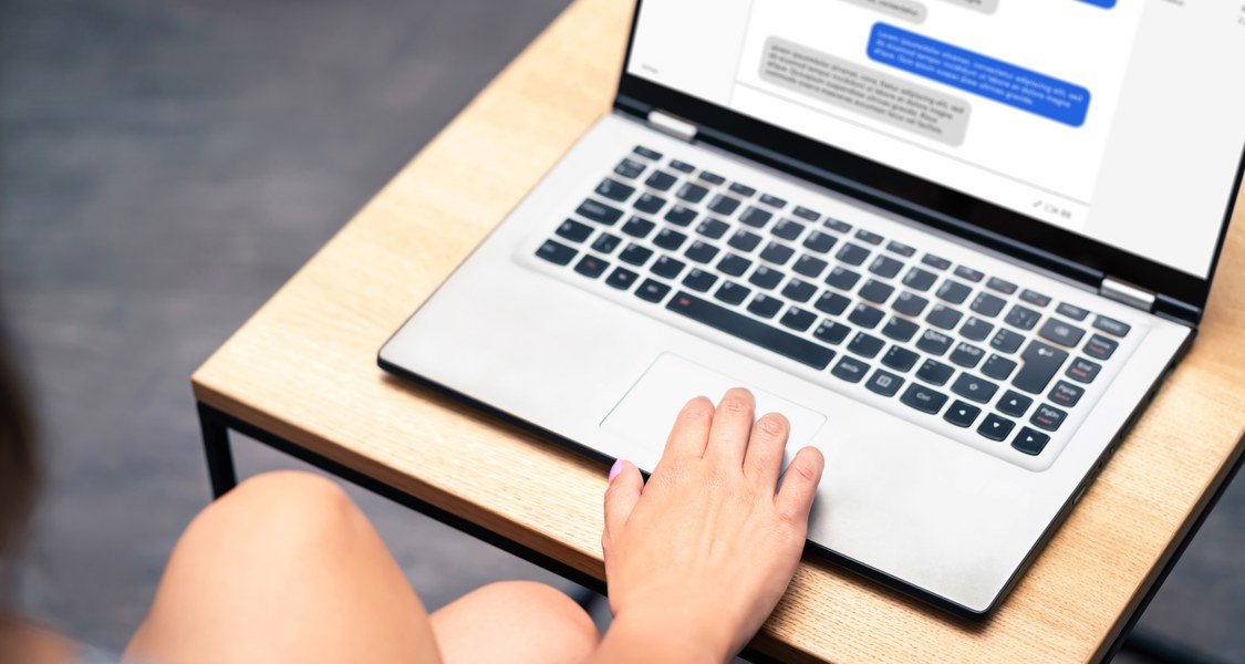 Eine Frau am Laptop. Auf dem Bildschirm ist verschwommen ein Chatverlauf zu sehen.