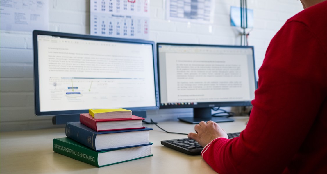 Ein Schreibtisch, mit PC und einem Bücherstapel