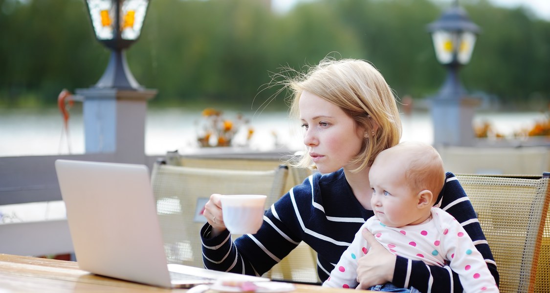 Frau mit Kind auf dem Schoß sitzt am Laptop.