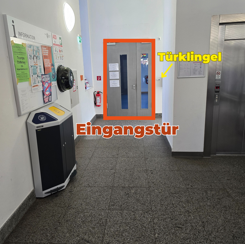 Ein Foto des Erdgeschosses der Bahnhofstraße 7. Zu sehen ist an der hinteren Wand die Eingangstür der ADiS, rechts daneben ist die Türklingel farblich markiert. An der linken Wand steht ein Mülleimer, auf der rechten Seite ist etwas weiter vorne ein Aufzug.