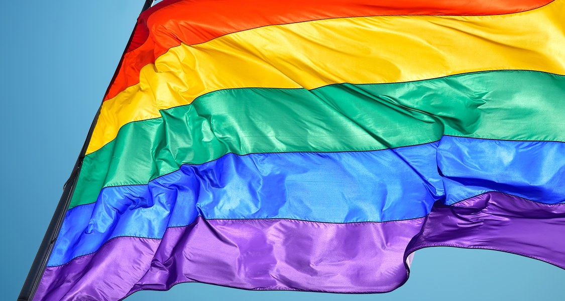 Eine wehende Regenbogenflagge vor einem strahlend blauen Himmel.