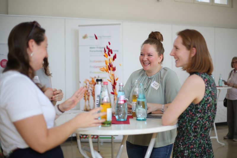 Mentees stehen um einen Bistrotisch und tauschen sich gut gelaunt aus.