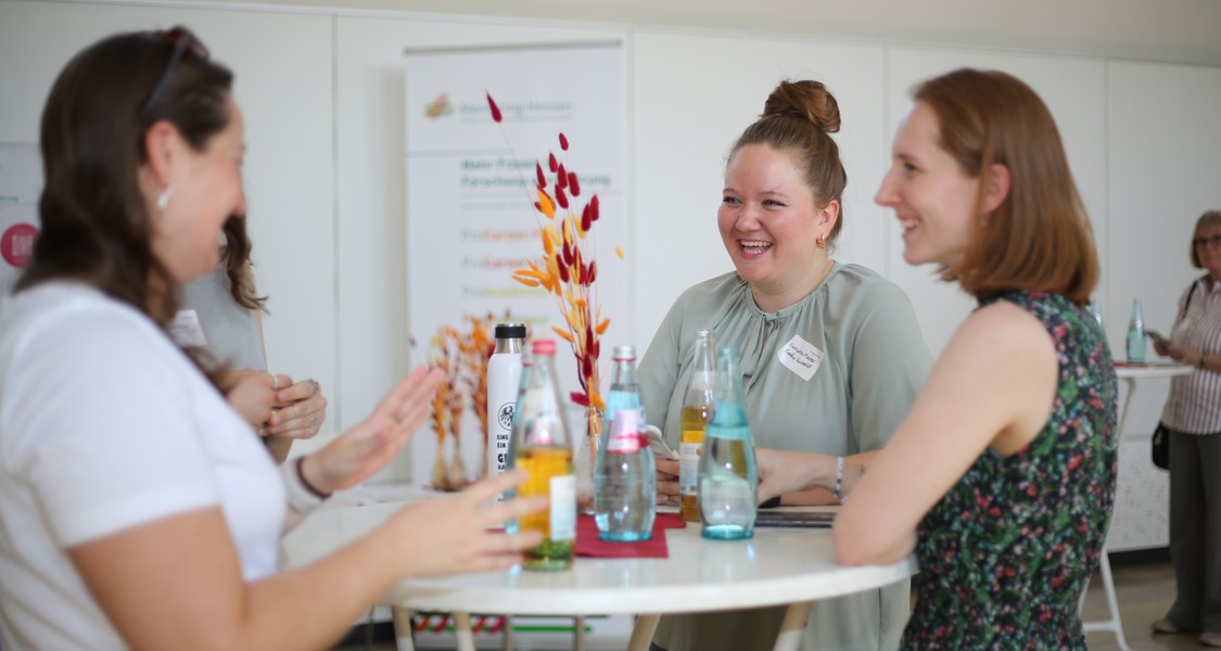 Mentees stehen um einen Bistrotisch und tauschen sich gut gelaunt aus.