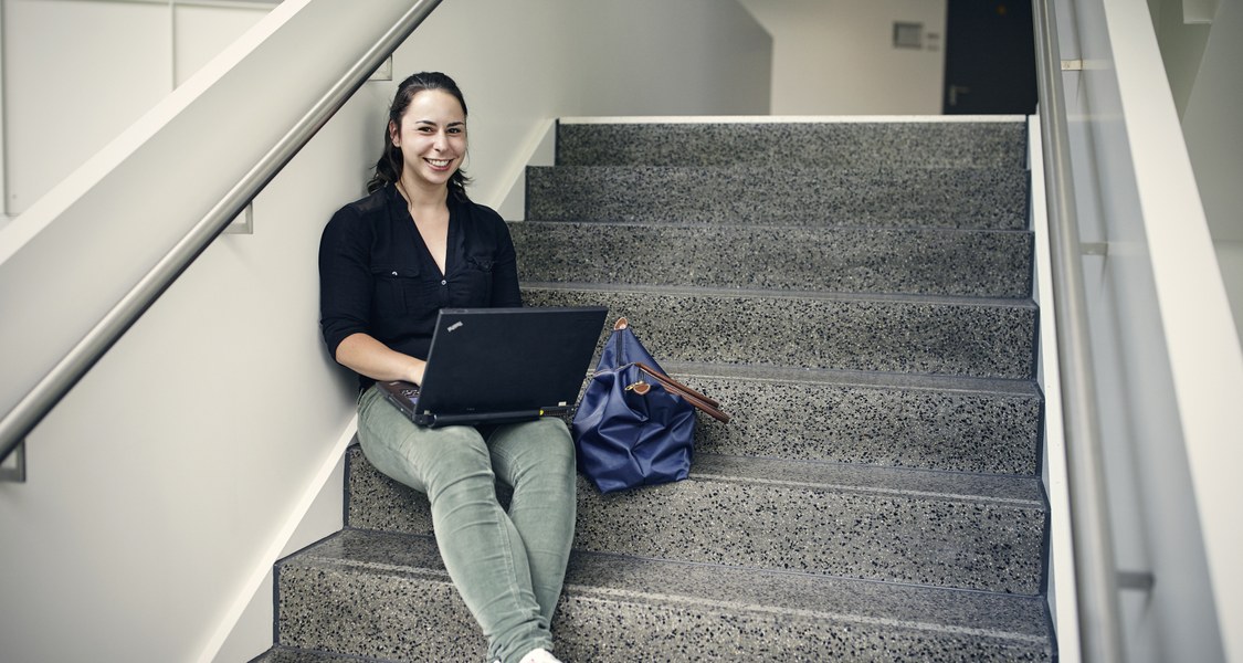 Studentin sitzt auf Treppe und lernt mit Laptop