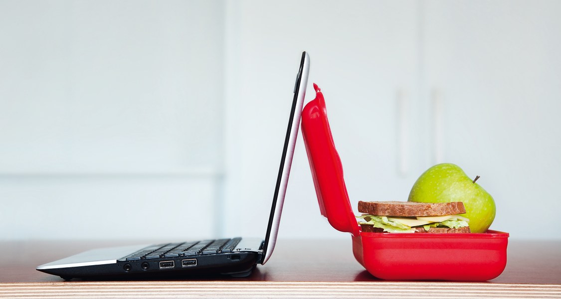 Ein aufgeklappter Laptop und eine aufgeklappte Brotdose stehen zusammen auf einem Tisch