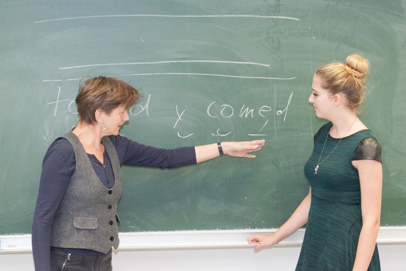 Lehrende und Studentin erörtern an der Tafel