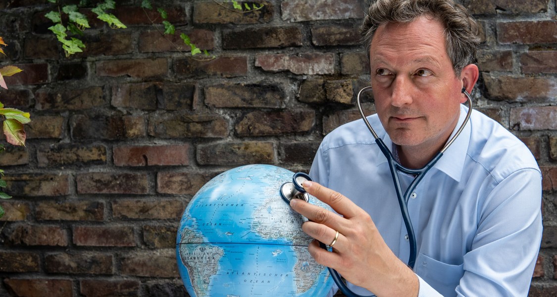 Dr. Eckart von Hirschhausen hält einen aufblasbaren Globus in den Händen und hört ihn mit einem Stetoskop ab, als würde er seine Gesundheit prüfen.