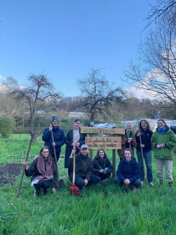 Eine Gruppe von Menschen steht vor einem Beet und einem Schild der Urban-Gardening-Gruppe "Wurzel(t)räume"