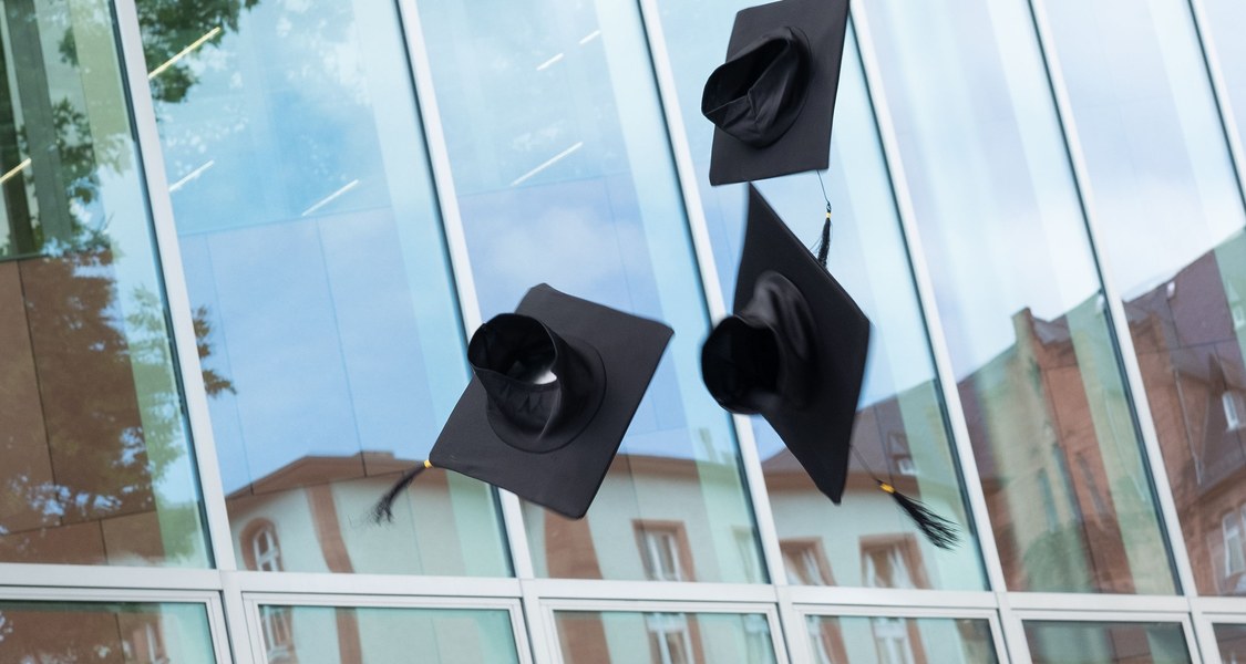 Doktorhüte fliegen vor der Fassade der neuen Universitätsbibliothek