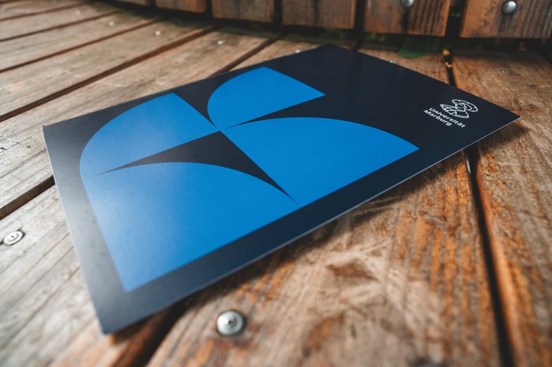 dunkelblaue Tagungsmappe mit vier mittelblauen Viertelkreisen und dem Uni-Logo (stilisierter Philipp mit Schriftzug Universität Marburg)