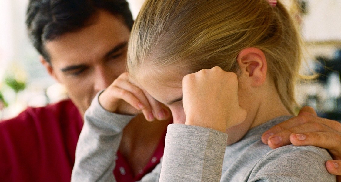 Ein trauriges Schulkind wird von einer Lehrkraft getröstet.