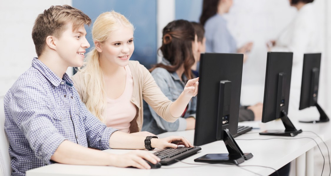 Eine junge Frau und ein junger Mann sitzen vor einem Computer und gucken interessiert.