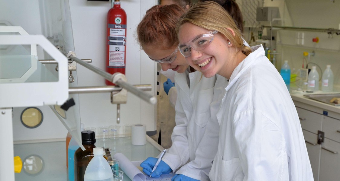 Zwei Teilnehmerinnen im Labor mit Kittel und Schutzmaske schreiben etwas auf ihre Klemmbretter